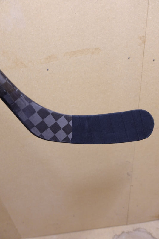 Close-up of the blade on Trevor Zegras' hockey stick with black tape job and checkered carbon graphic
