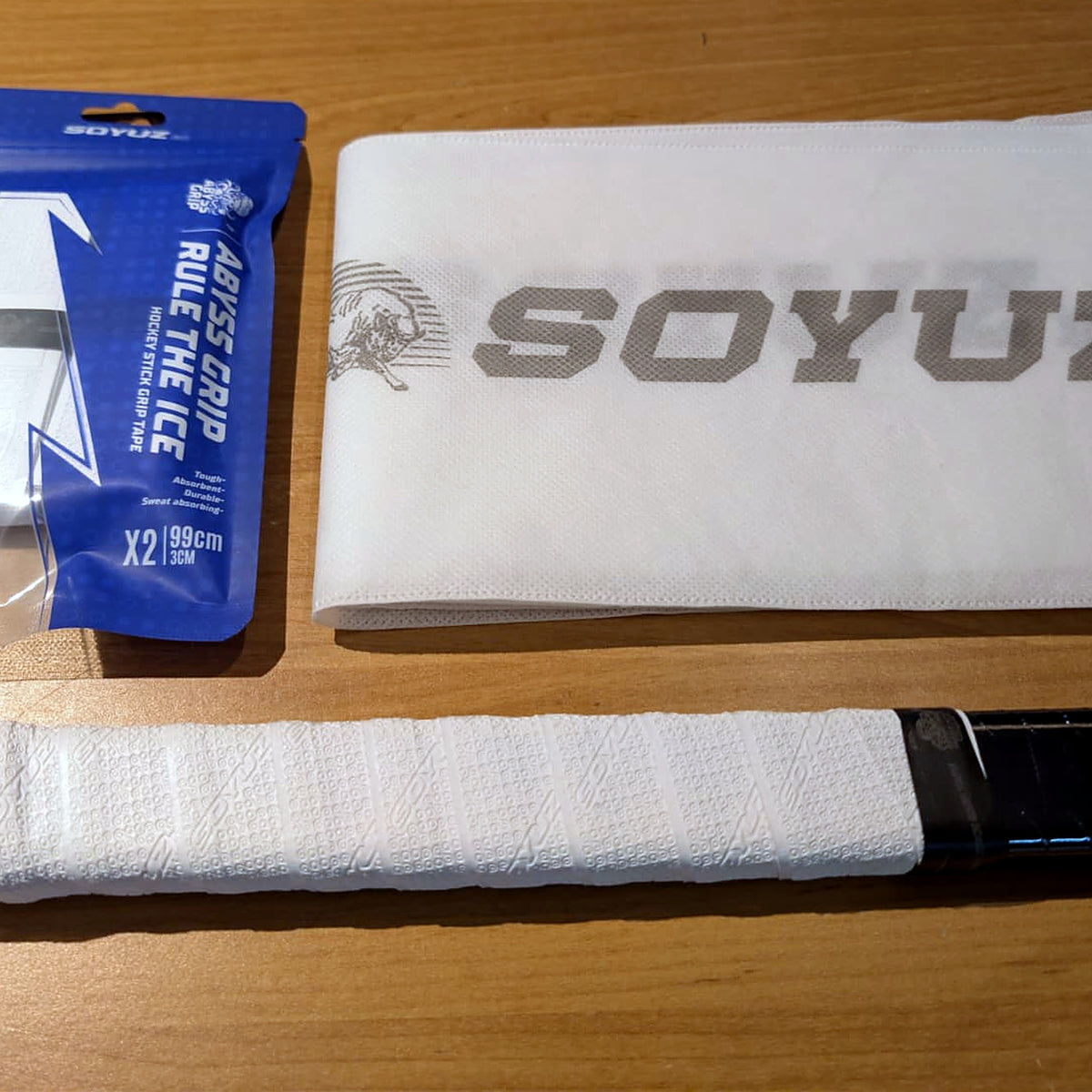 SOYUZ Griptape Verpackung neben einem Hockeyschläger mit weissem Griptape am Schaft