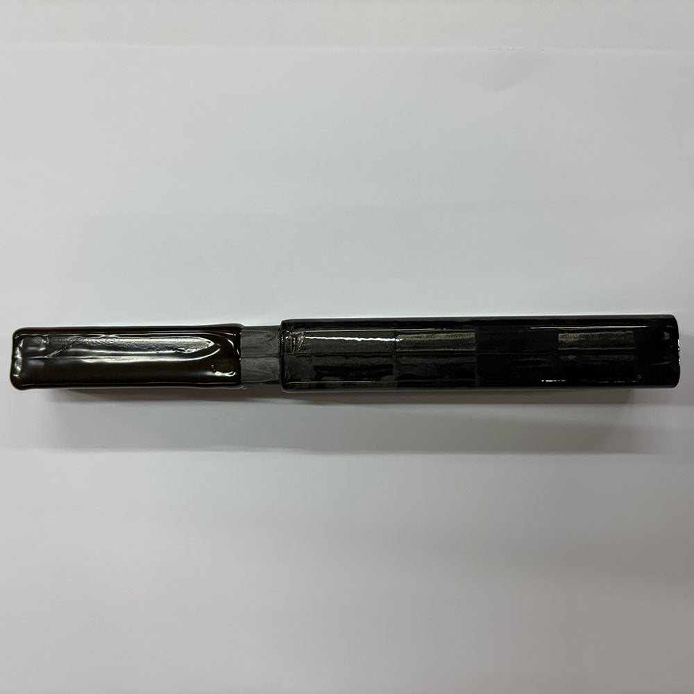 black 100 percent carbon stick extension. Black carbon pattern. Laid horizontally on a light grey table. Shadow pointing down